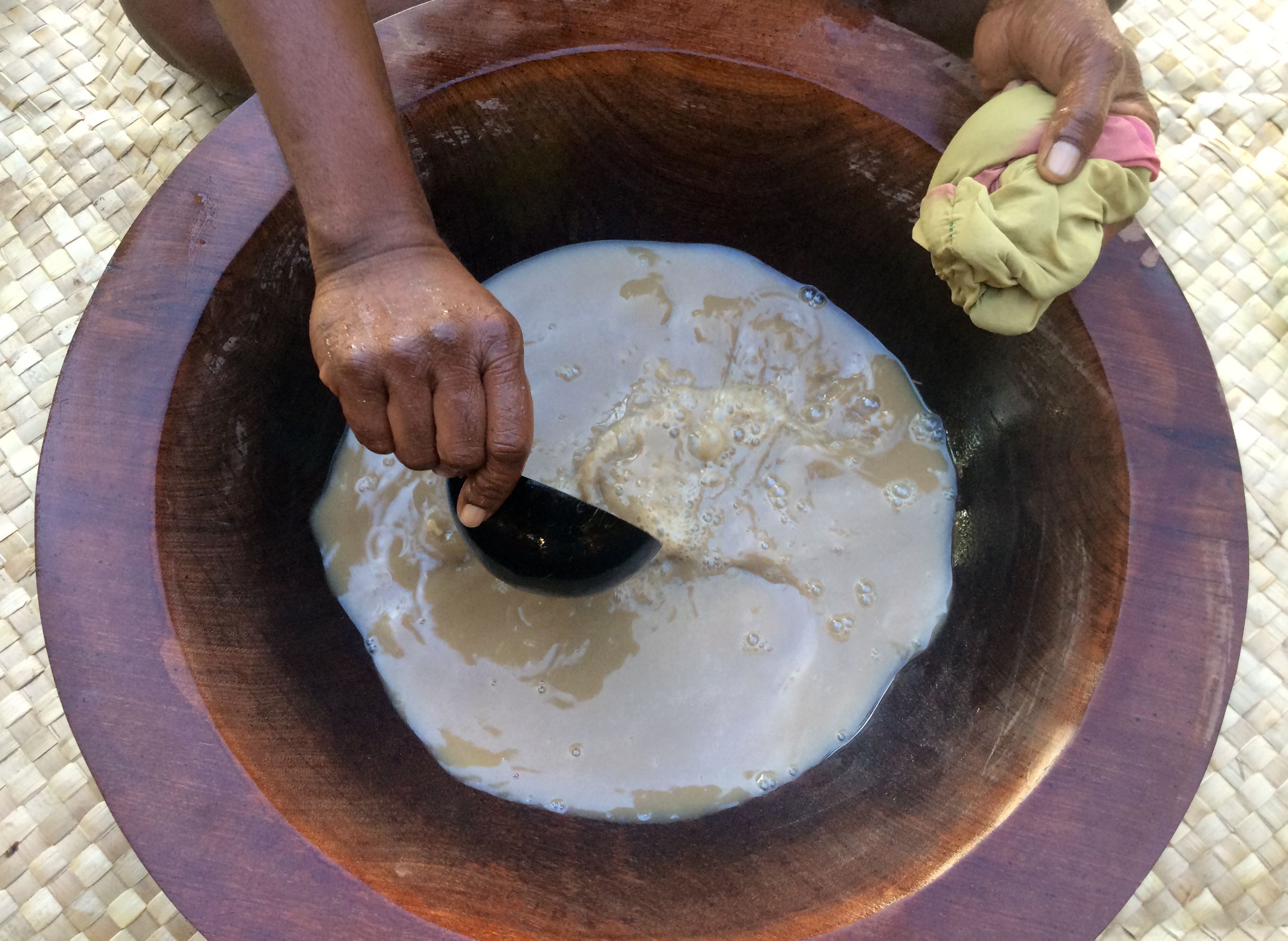 Ręce osoby przygotowującej tradycyjny, mlecznobiały napój kava kava w dużym, drewnianym naczyniu.