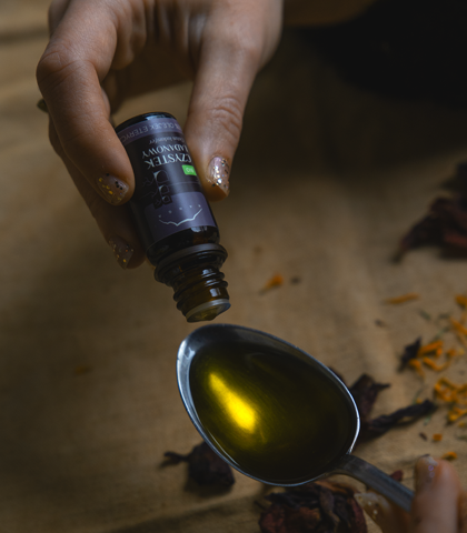 dłonie trzymają olejek eteryczny i dodają go na łyżkę z olejem bazowym