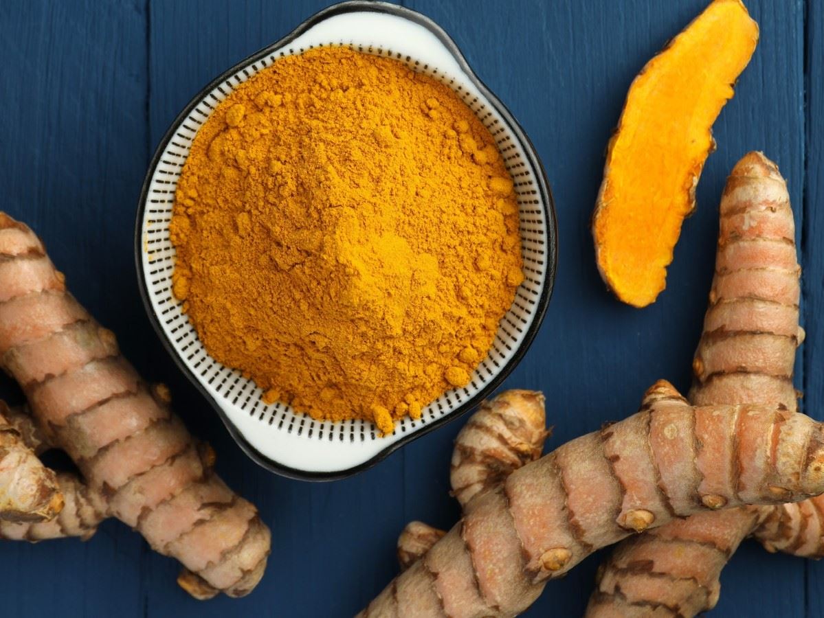 Intensywnie żółta, zmielona kurkuma w porcelanowej miseczce, obok jej prążkowane korzenie.