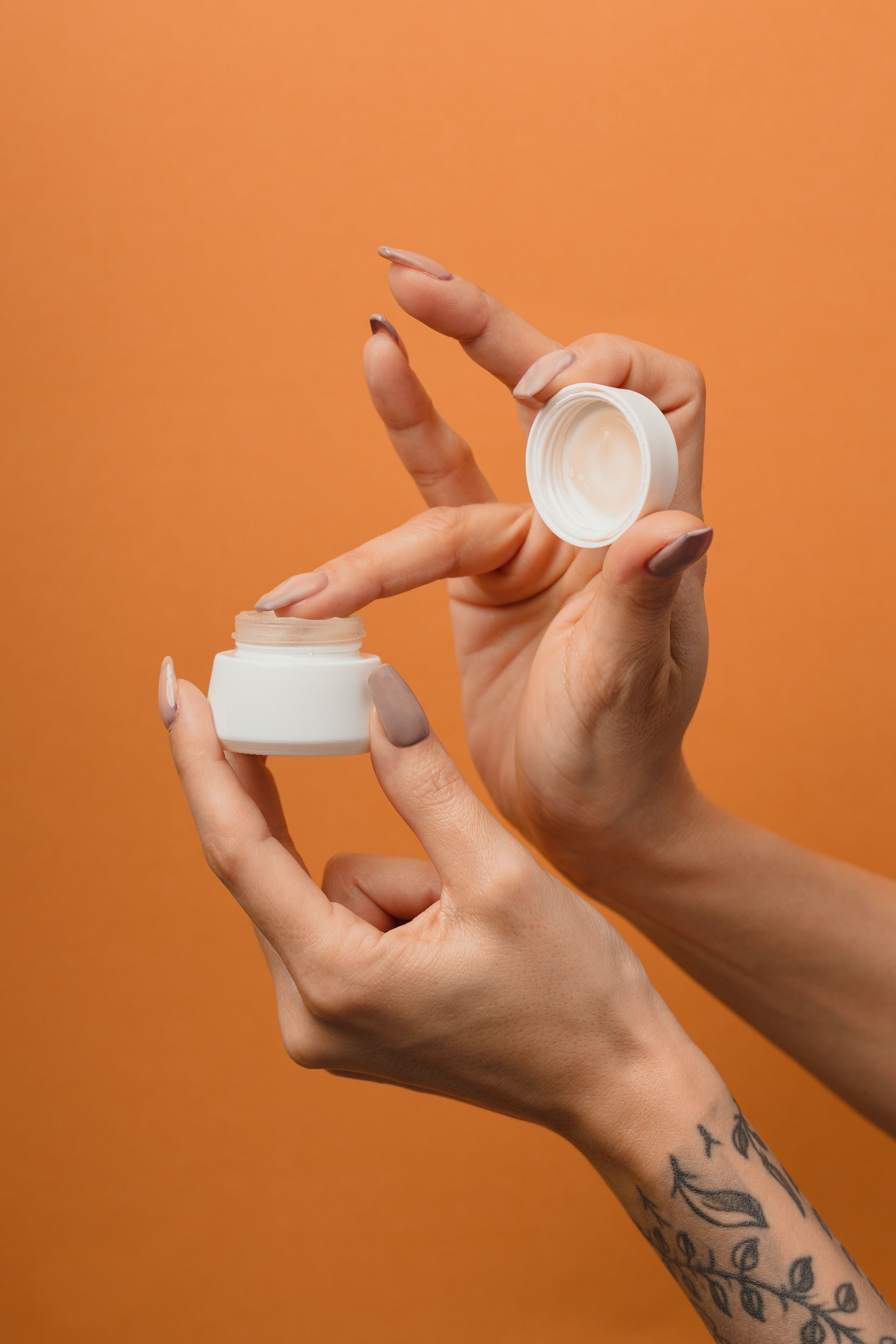 Kobieca dłoń nabierająca krem z małego słoiczka.