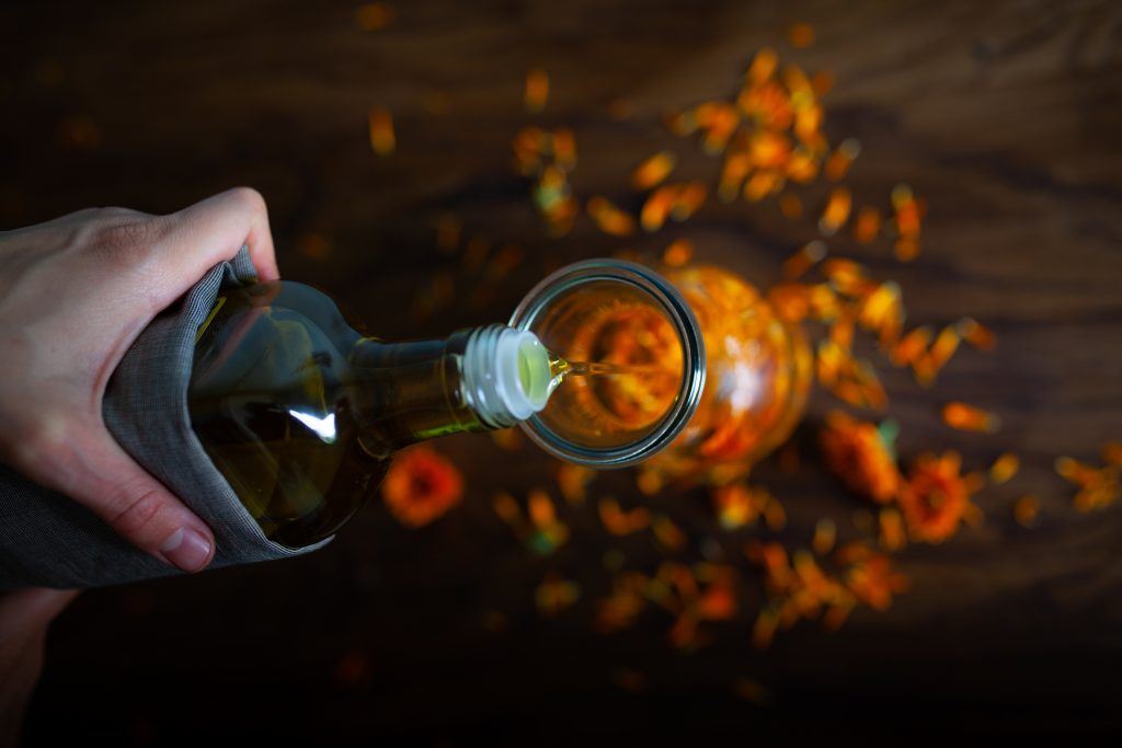 Olej wlewany do szklanej butelki z kwiatkami nagietka.