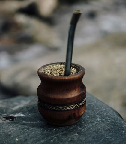 Drewniane naczynie z metalową bombillą wypełnione zmieloną yerba mate, umieszczone na kamieniu, przywodzi na myśl tradycyjny sposób parzenia naparu.