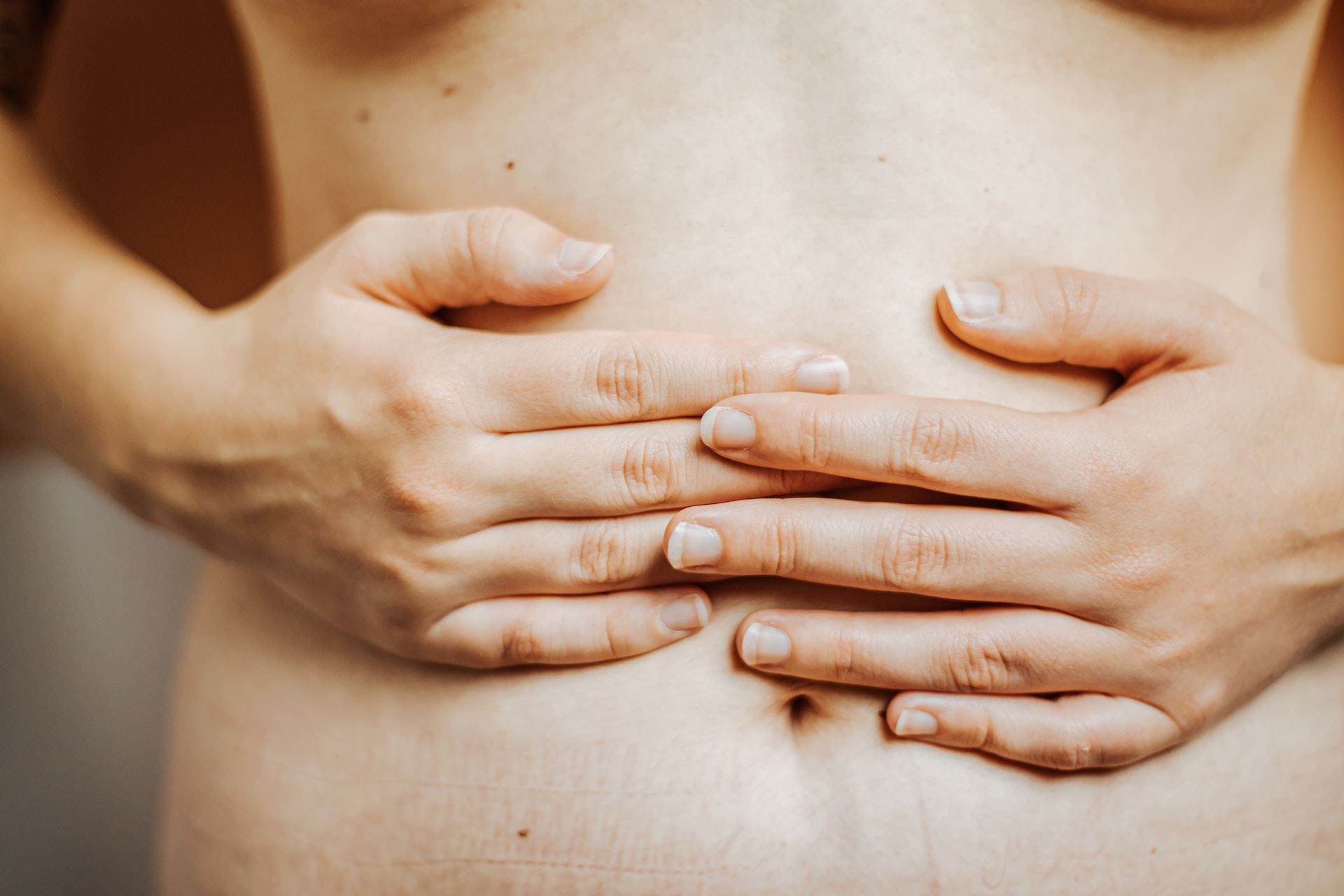 Kobieta obejmuje swój brzuch, gest troski o ciało.